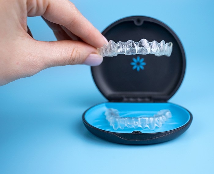 Fingers plucking Invisalign from its carrier case with light blue background