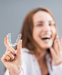 Woman holding out Invisalign laughing with gray background