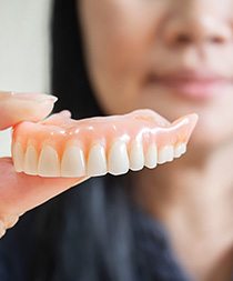 Close up of a senior woman holding full dentures in Gilbert, AZ