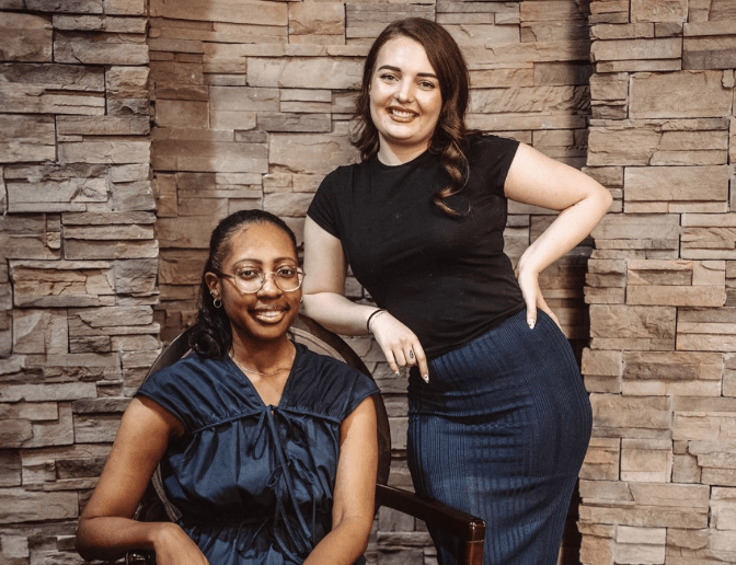Two smiling dental team members sitting at front desk