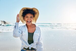 Woman in striped shirt and straw hat smiling at the beach